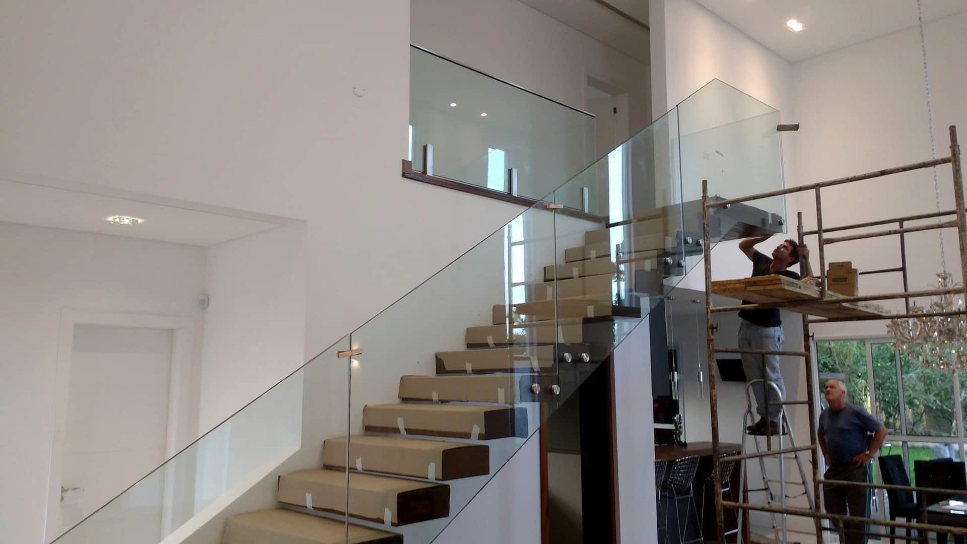 Instalação de guarda-corpo de vidro em escada, com andaime e equipe trabalhando