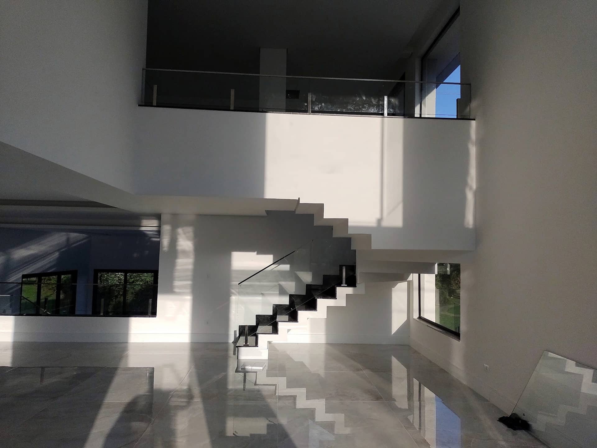 Sala com pé-direito duplo, escada em granito preto e mezanino com guarda-corpo de vidro